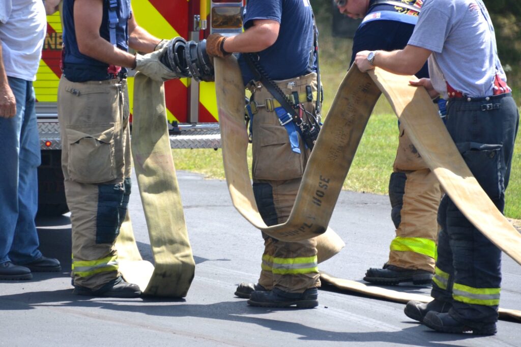 Firefighters helping other firemen with hose next to firetruck. True heroes doing community service.